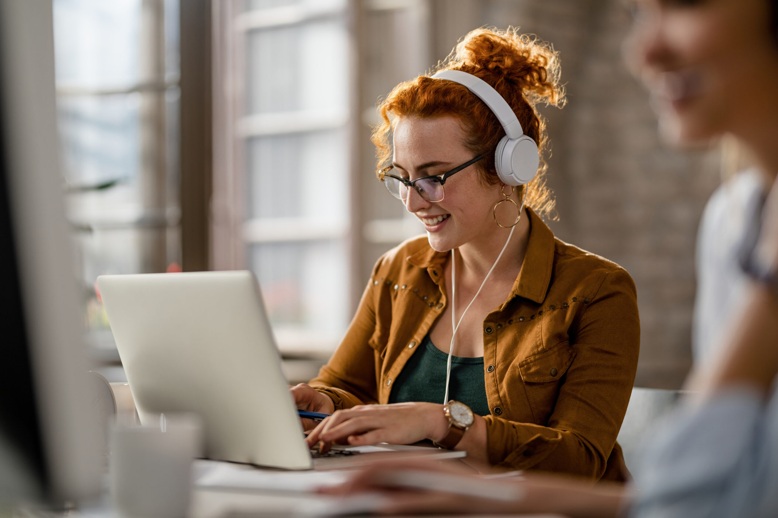 Happy freelance worker working on laptop while wearing headphone
